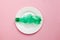 Plastic pollution of food concept, white plate with clean crumpled green plastic bottle isolated on pink