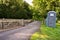 A plastic portable toilet next to a covered cattle grid on a public footpath in a field at an outdoor event