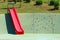 Plastic red slide next to children climbing wall at local playground with climbing wall holds in various shapes and climbing ropes