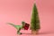 Plastic toy dinosaur with  present box against evergreen tree on a pink background