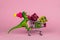 plastic toy dinosaur wearing tiny knitted hat and driving shopping trolley full of present boxes on a pink background ,