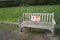 Plastic warning sign tied to a Woden public bench advising people to maintain social distancing to avoid the spread of Covid-19