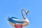 Plastic white-blue swan with a crown. Blue background.