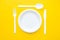 Plastic white fork, knife, spoon and plate on yellow background. Cooking utensil. Top view. Minimalist Style. Copy, empty space