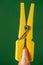 plastic yellow clothes peg pinching hand index finger under green background