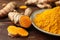 Plate with aromatic turmeric powder and cut roots on wooden table, closeup