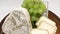 A plate of assorted mouldy goat`s milk cheeses on a wooden Board with green grapes