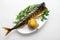 Plate with baked mackerel stuffed with herbs, onions and boiled potatoes with spices and butter on a textured gray background,
