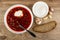 Plate of borscht with sour cream, spoon, bowl with sour cream, garlic, piece of bread on table. Top view
