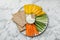 Plate with crispbreads, vegetable sticks and dip sauce on white marble table, top view