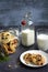 Plate with delicious homemade cookies, a glass jar, a bottle and glasses with milk on a dark gray background