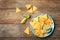 Plate with delicious mexican nachos chips, guacamole  and lime on wooden table, flat lay. Space for text
