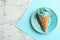 Plate with delicious spirulina ice cream cone on marble table, top view.