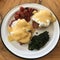 A plate of Eggs Benedict with fried cherry tomatoes and greens on a white plate