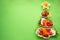 Plate in the form of a Christmas tree with vegetables, fruits, mushrooms and berries.Green background. The concept of vegetarian
