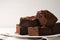 Plate with fresh brownies on white table against light background. Delicious chocolate pie