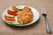 Plate with fried meat chop in batter and sliced tomato and cucumber with fork