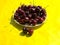 Plate full of ripe red cherries on yellow background close-up. Summer concept. Copy space