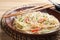 Plate of hot noodles with broth, vegetables and chopsticks on table