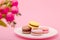 Plate of macaroons on pink background with flowers. Sweet pastry, baked products, sweets, dessert. Unhealthy diet, sugar