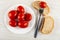 Plate with marinated tomatoes, tomato strung on fork on piece of bread, pieces of bread on table. Top view