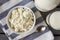 Plate of natural cottage cheese, a glass of cow`s milk,  bottle of milk, spoon,  striped towel on a gray background