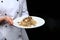 A plate of pasta and black truffle in the hands of the chef. Unrecognizable person. Photo on a black background