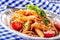 Plate with pasta pene Bolognese sauce cherry tomatoes parsley top and basil leaves on checkered blue tablecloth.