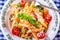 Plate with pasta pene Bolognese sauce cherry tomatoes parsley top and basil leaves on checkered blue tablecloth.