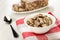 Plate with piece of sunflower halva with cocoa, spoon, bowl with pieces of halva on napkin on wooden table