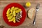 Plate with pieces of canned herring and fried potato, pepper, piece of bread, fork on table. Top view