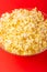 A plate with popcorn on a red background. The concept of film viewing, rest at the weekend