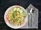 plate of pork fried rice is on a brown wooden table and there are utensils placed beside it. Fast food