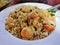 plate of pork fried rice is on a brown wooden table and there are utensils placed beside it. Fast food