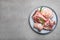 Plate with raw chopped meaty bones and basil on grey table, top view. Space for text