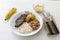 Plate of rice, beans, steak and cassava. With cutlery and manioc flour and banana for dessert.