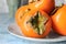 Plate with ripe persimmons on table, closeup