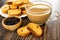 Plate with rusks, bowl with dried grape, transparent cup of coffee with milk on wooden table