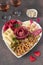 Plate shaped-heart for Valentines Day with varieties sausage, cheese, walnuts, olives and two glass rose wine on brown