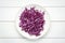 Plate with shredded fresh red cabbage on white wooden table, top view