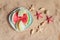 Plate with slices of melon and watermelon, starfishes and seashells on sand beach.