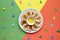 Plate of small round pancakes with colorful party topper flags on split three color layered paper background. Top view