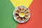 Plate of small round pancakes with colorful party topper flags on split three color layered paper background. Top view