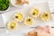 Plate of spring flower shaped lemon tarts with bees, top view scene against a white wood background