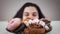 Plate with sweets standing on the table, obese Caucasian woman appearing from under the table and smiling. Hungry fat