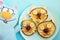 A plate with three pancakes in the shape of cat faces, decorated with slices of banana, grape and apple and a soft toy cat with an