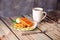 A plate with waffles in cream and slices of banana and kiwi, next to a mug of coffee on a wooden table against a gray wall