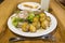 A plate with young potatoes and meat is standing on a tray