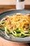 Plate with zucchini spaghetti, mushrooms and cheese on wooden board, closeup