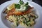 Plated fish entree wither herb butter on a bed of risotto and greens with lemon garnish